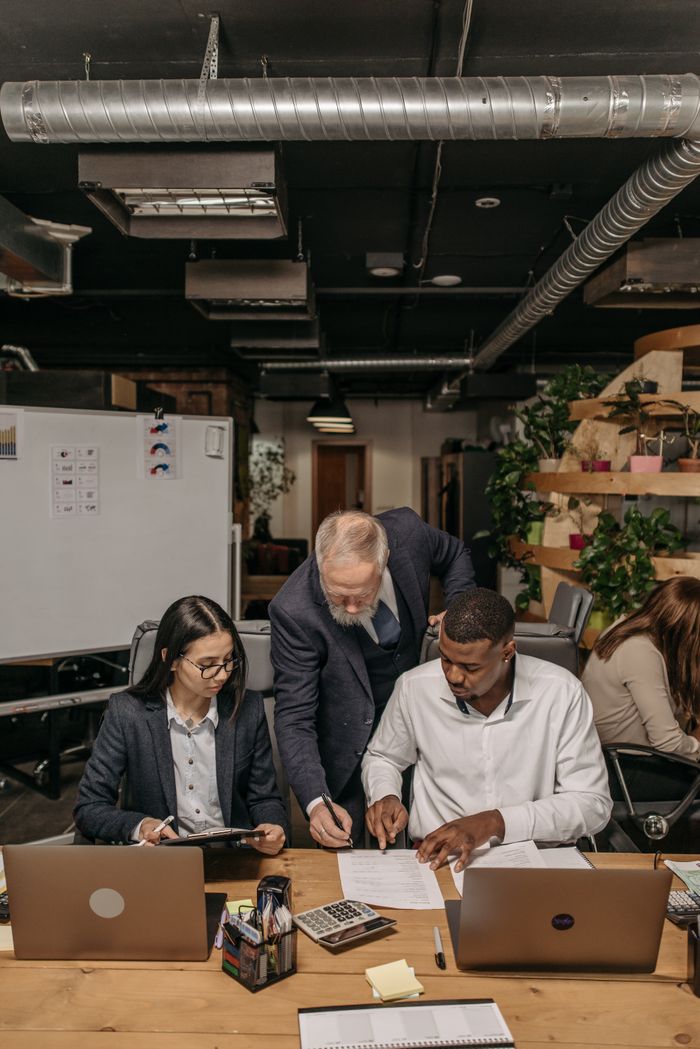 A diverse team collaborating at a table with laptops and documents in a modern office environment.
